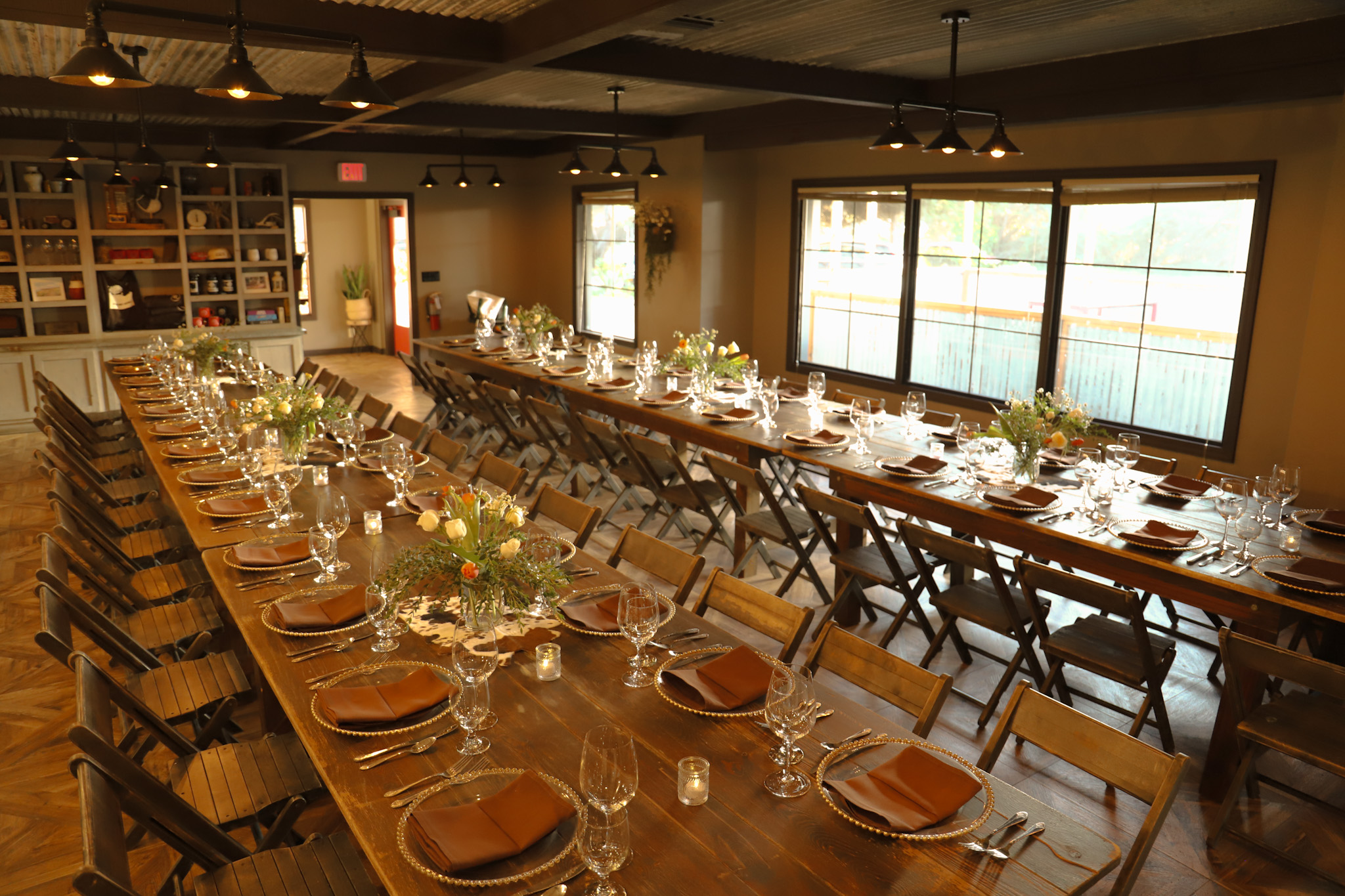 A long dining table set with plates, glasses, and flowers in a room with windows.