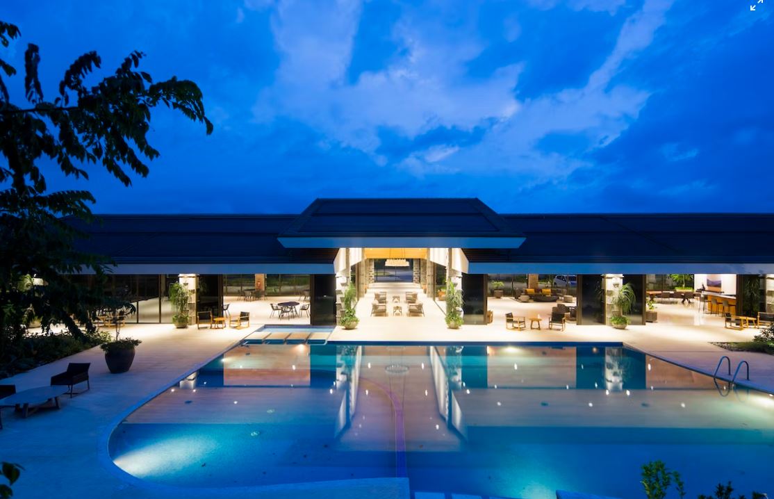 A hotel exterior with a pool and outdoor seating area at dusk.