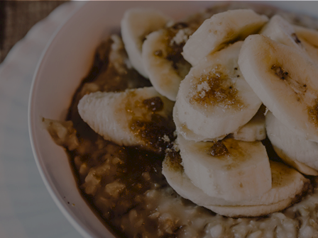 A bowl of oatmeal topped with banana slices and a drizzle of brown sugar or syrup, creamy and comforting.
