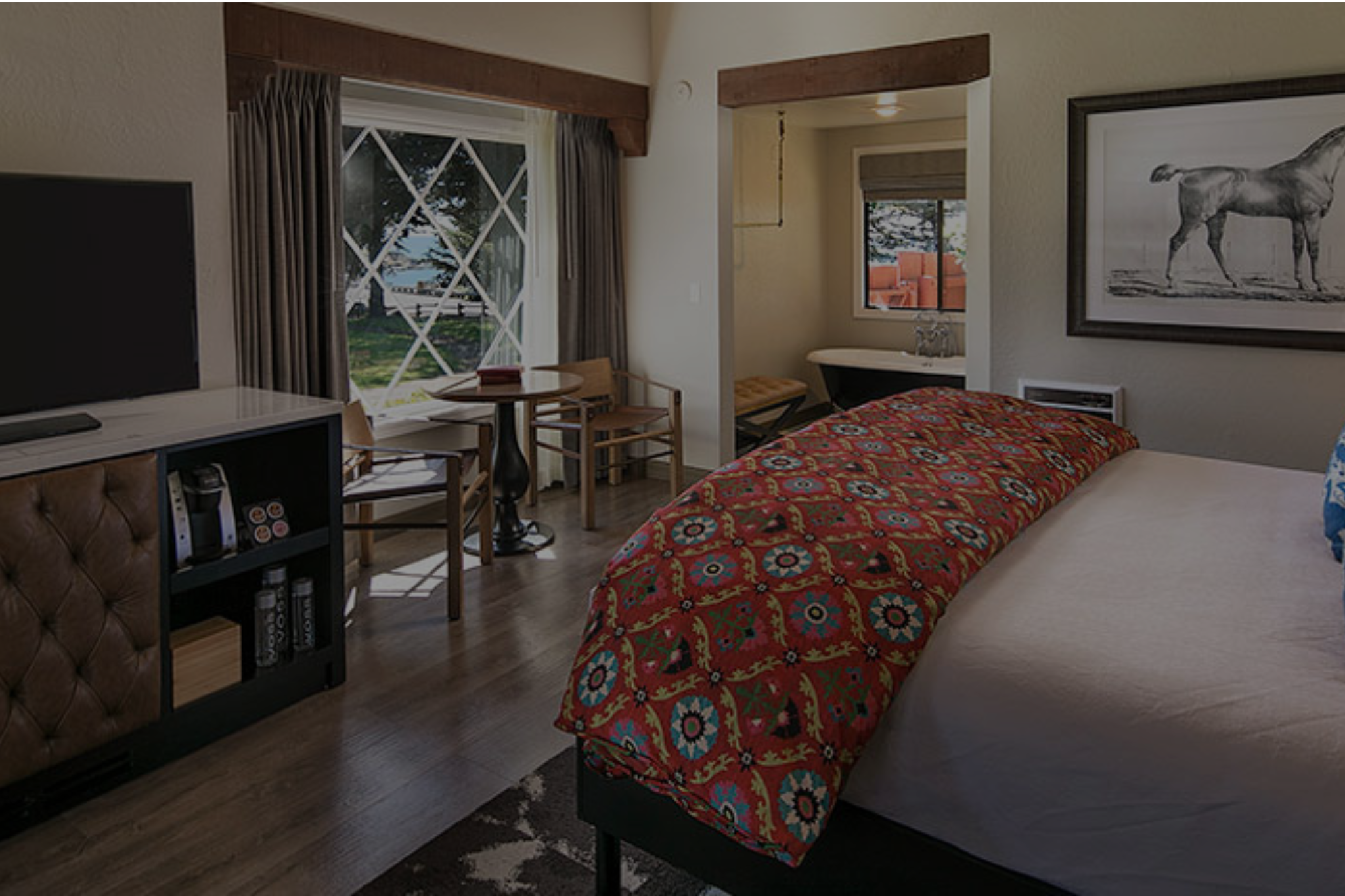 A wide view of a hotel room with a bed, TV, table, and window.