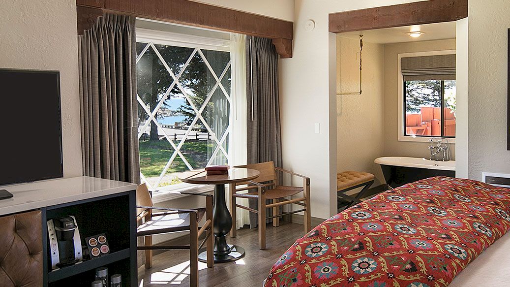 A hotel room with a large bed, patterned red comforter, flat-screen TV, dresser, seating area, and a framed horse drawing on the wall.