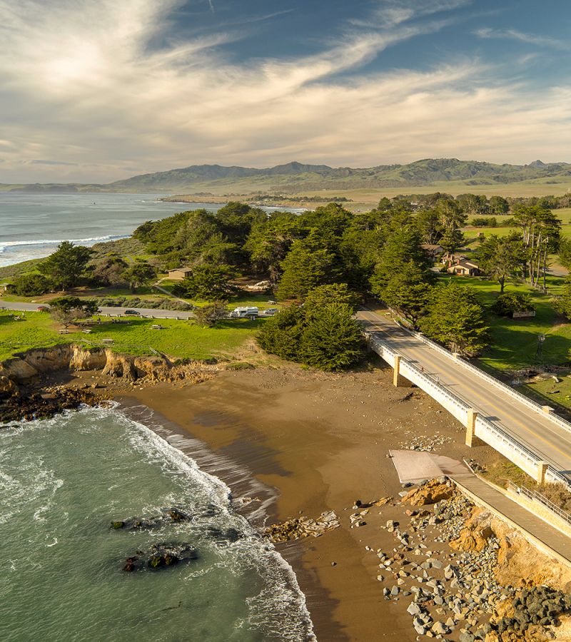 Aerial view of a coastal landscape with a bridge, beach, and trees.