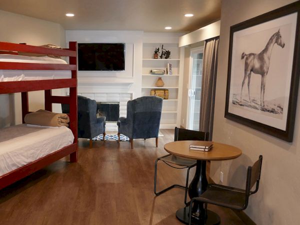 A compact living space with a bunk bed, cozy seating by a fireplace, a round table and chairs, and a large horse print on the wall.