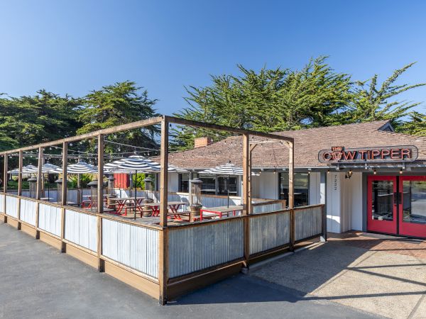 A small outdoor-style restaurant with a wooden-framed fenced patio, red doors, and a sign that reads &ldquo;Wavv&hellip;,&rdquo; sunny day and blue sky.