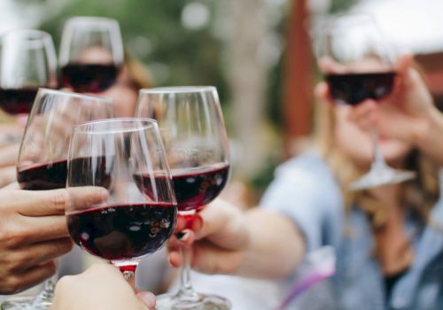 A group of people clinking glasses of red wine in a toast, cheers all around, outdoors.