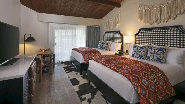 A hotel room with two beds, a desk, and a TV