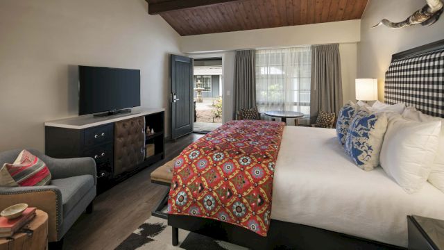 A hotel room with a large bed, TV, sofa, and window