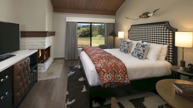 A wide view of a hotel room with a large bed, fireplace, and window showing a view.