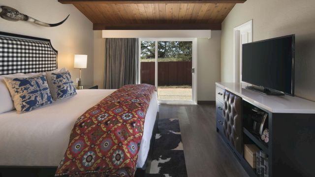 A wide view of a hotel room with a king-sized bed, a TV on a stand, and a sliding glass door leading to an outdoor area.