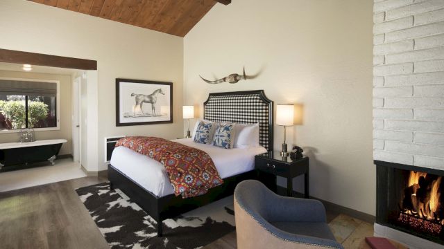 A wide view of a guest room with a king-sized bed, fireplace, and a tub in the bathroom in the background.