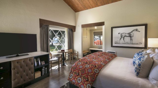 A wide-angle view of a hotel room with a large bed, dresser, TV, dining table, and chairs.