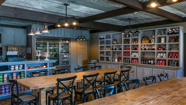 A dining area with wooden tables and metal chairs, shelves with products, and a kitchen counter.