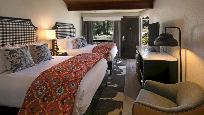 A wide view of a hotel room with two double beds, a desk, chair, and window.