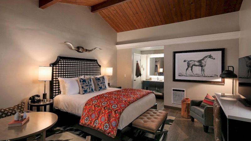 A wide view of a hotel room with a bed, nightstand, lamp, TV, chair, and desk.