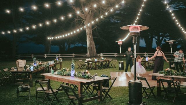 An outdoor event space set up for a nighttime gathering with string lights, tables, chairs, and heaters.