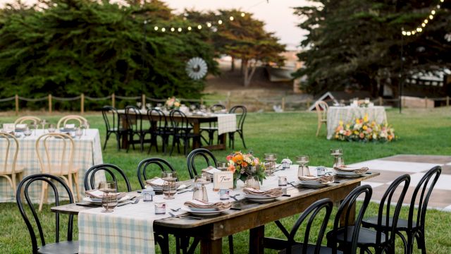 An outdoor dining area set with tables, chairs, and flowers under string lights.