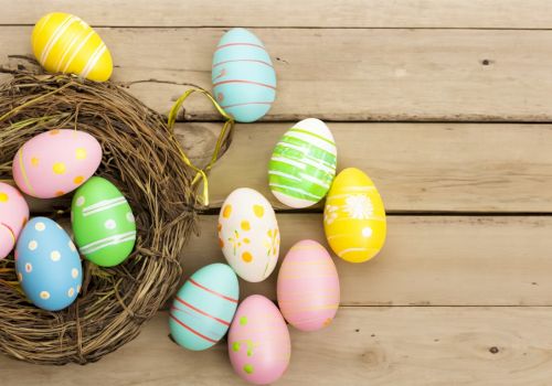 Colorful Easter eggs in a nest on a wooden surface, with pastel patterns and polka dots, bright and cheerful.