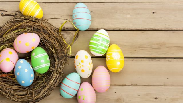 Colorful Easter eggs in a nest on a wooden surface, with pastel patterns and polka dots, bright and cheerful.