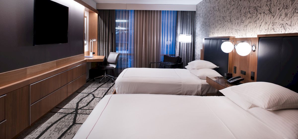 A hotel room with two beds, a desk, a TV, and a marble wall