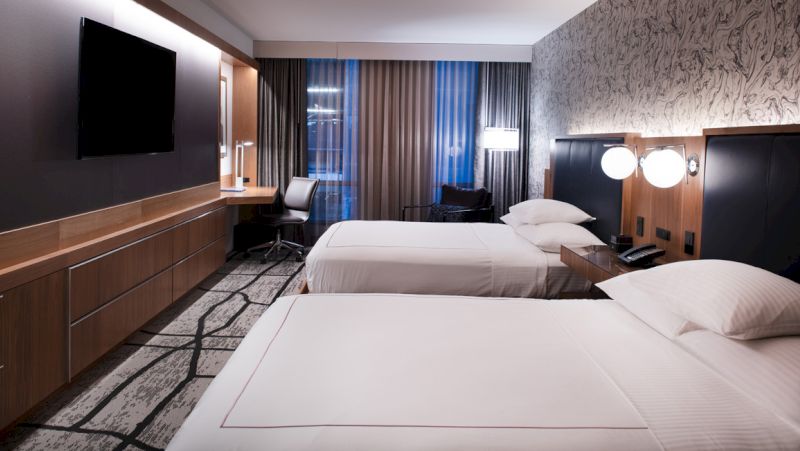A hotel room with two beds, a desk, a TV, and a window.